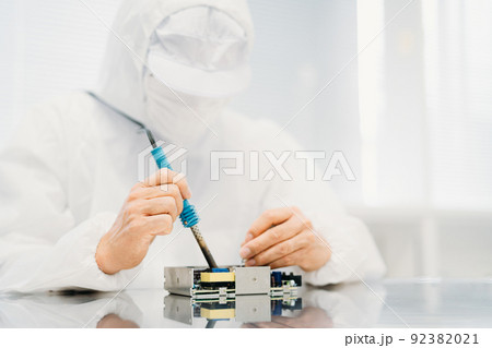 工場のクリーンルームでハンダ付けする防塵服を着た男性(電子部品) 工場のクリーンルームでハンダ付けする防塵服を着た男性(電子部品) 92382021