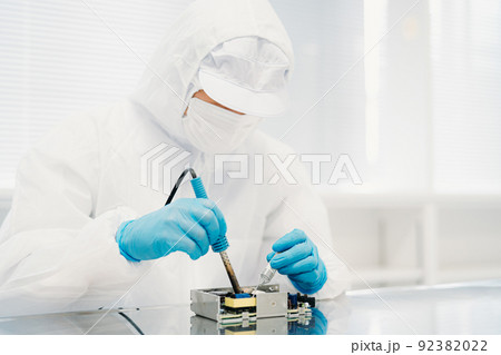 工場のクリーンルームでハンダ付けする防塵服を着た男性（電子部品） 92382022