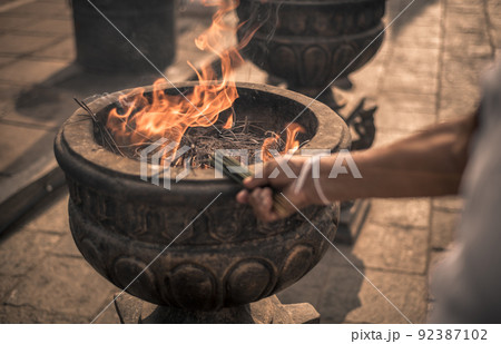 New incense sticks getting lit up by the woman's hand, Burning incense sticks in the old stone pot at Sacred Sri Maha Bhodi Gardens. New incense sticks getting lit up by the woman's hand, Burning incense sticks in the old stone pot at Sacred Sri Maha Bhodi Gardens. 92387102