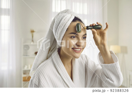 Beautiful young woman doing face massage with facial roller for better blood circulation 92388326