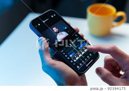 the video editor program on the phone. A young man is editing a video on his phone the video editor program on the phone. A young man is editing a video on his phone 92394175