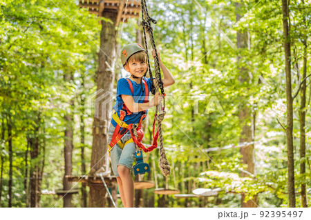 Happy child in a helmet, healthy teenager school boy enjoying activity in a climbing adventure park on a summer day Portrait of a disgruntled girl sitting at a cafe table Happy child in a helmet, healthy teenager school boy enjoying activity in a climbing adventure park on a summer day Portrait of a disgruntled girl sitting at a cafe table 92395497