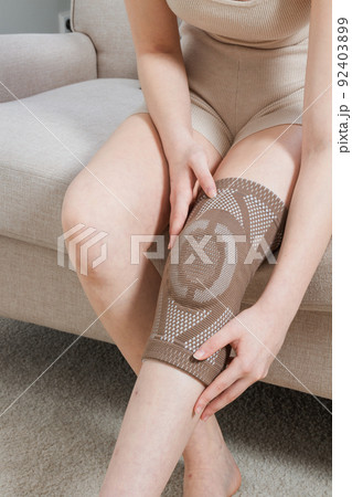 Knee support brace on a woman leg. girl in an orthosis in the interior of the house. Orthopedic anatomic braces for knee fixation, injuries and pain. Knee Joint Bandage Sleeve. Elastic Sports. Knee support brace on a woman leg. girl in an orthosis in the interior of the house. Orthopedic anatomic braces for knee fixation, injuries and pain. Knee Joint Bandage Sleeve. Elastic Sports. 92403899