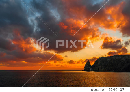 A gold burning sunset with the silhouette of a rocky cape over the sea. Summer ocean sea beach background. Nobody. Holiday, vacation and travel concept 92404074