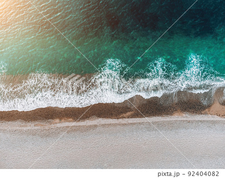 Aerial view from above on azure sea and pebbles beach. Small waves on cristal clear water surface in motion blur. Nature summer ocean sea beach background. Nobody. Holiday, vacation and travel concept 92404082
