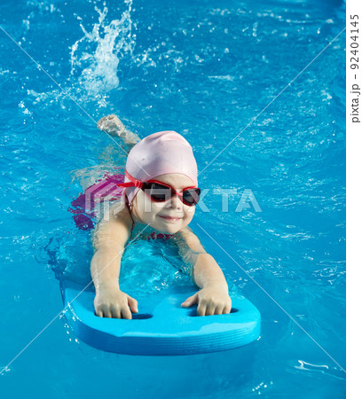 Little girl learning to swim in indoor pool with pool board 92404145