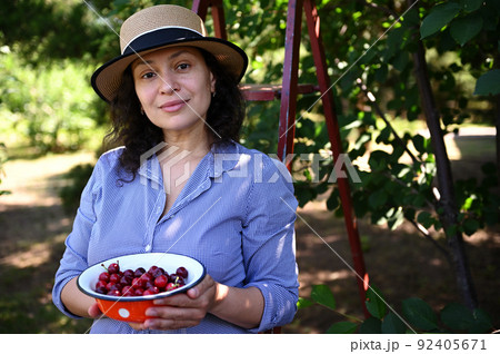 Beautiful woman, eco farm owner, gardener showing freshly picked cherries in her organic garden. Agribusiness. Farming 92405671