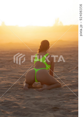 Seductive model in swimsuit kneeling on sandy beach 92406356