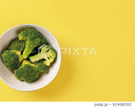 Raw green broccoli florets in a bowl against yellow background. Raw green broccoli florets in a bowl against yellow background. 92406502