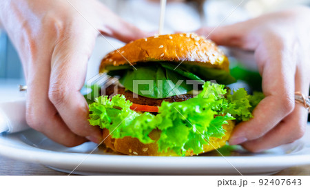Vegan sandwich healthy vegetarian burger. Cute cheerful girl eating veggie hamburger with salad, avocado, vegetable. Vegetarian diet food concept. Vegan sandwich healthy vegetarian burger. Cute cheerful girl eating veggie hamburger with salad, avocado, vegetable. Vegetarian diet food concept. 92407643