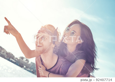 Outdoors photo of happy boyfriends piggybacking their girlfriends at sunset on beach Outdoors photo of happy boyfriends piggybacking their girlfriends at sunset on beach 92407714