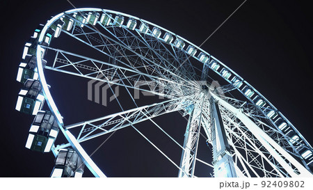 Brightly lit ferris wheel ride, which spinning at night or evening carnival. Low angle. Colored 92409802