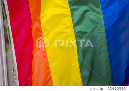 Close Up rainbow gay pride flag outside on a street. Symbol of the Lesbian Bisexual Transgender LGBT community waving in wind against cloudy sky. Social movement for freedom and equliaty. Copy Space 92410356