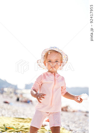 Little girl in a panama hat stands on a beach 92417955