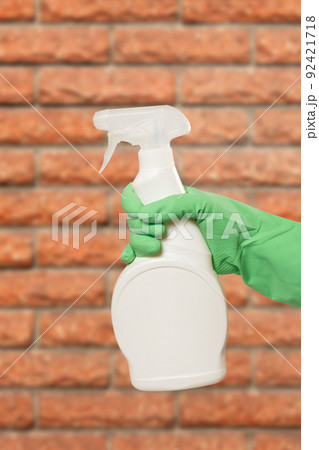 Woman's hand in protective glove with bottle of cleaning liquid. Woman's hand in protective glove with bottle of cleaning liquid. 92421718