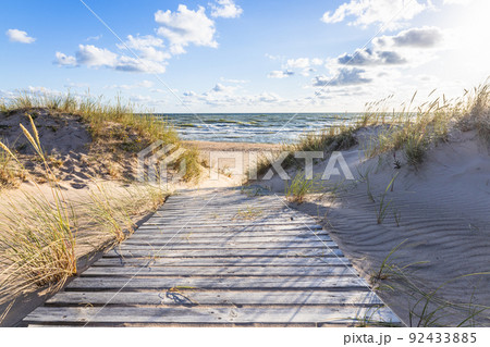 The path through dunes to the sandy beach on the Baltic Sea in summer with a blue sky The path through dunes to the sandy beach on the Baltic Sea in summer with a blue sky 92433885