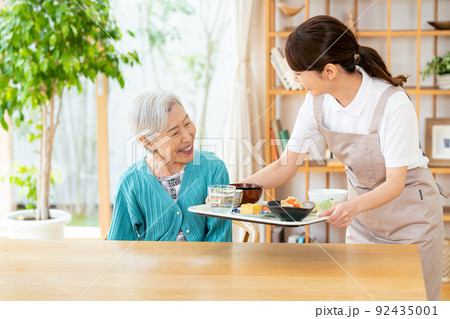 食事するシニア女性とヘルパーの女性 92435001