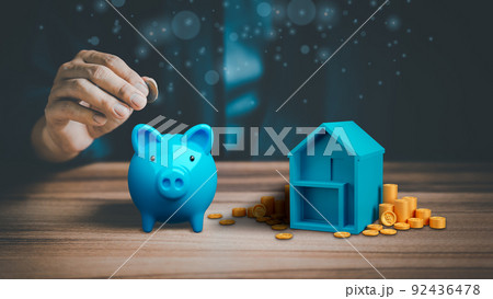 Man hand putting money coin into blue piggy bank for saving money, concept of saving to buy a house, real estate or home. Man hand putting money coin into blue piggy bank for saving money, concept of saving to buy a house, real estate or home. 92436478