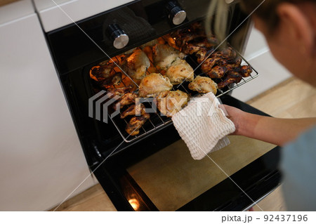 Woman cook taking out baked chicken from oven on baking sheet closeup Woman cook taking out baked chicken from oven on baking sheet closeup 92437196