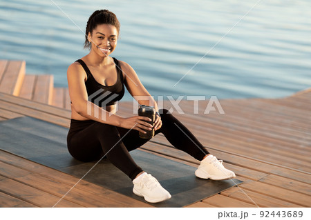 Cheerful african american athletic woman drinking water, exercising outdoors 92443689