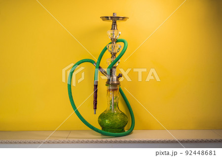 hookah shisha with glass flask and metal bowl with colored smoke on a yellow background. Traditional Eastern vacation for relaxation 92448681