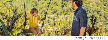 Young boy swinging in the jungle rainforest of Bali island, Indonesia. Swing in the tropics. Swings - trend of Bali. Traveling with kids concept. What to do with children. Child friendly place BANNER Young boy swinging in the jungle rainforest of Bali island, Indonesia. Swing in the tropics. Swings - trend of Bali. Traveling with kids concept. What to do with children. Child friendly place BANNER 92451173