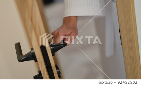 Woman hand in bathrobe opens and closes bathroom door 92452502