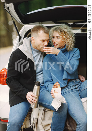 Romantic couple sitting in a trunk of white car in a forest with a tea and croissants 92454215
