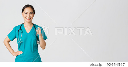 Covid-19, healthcare workers, pandemic concept. Confident smiling asian professional doctor, nurse in scrubs pointing finger at camera, inviting for check-up or vaccination, give recommendation Covid-19, healthcare workers, pandemic concept. Confident smiling asian professional doctor, nurse in scrubs pointing finger at camera, inviting for check-up or vaccination, give recommendation 92464547