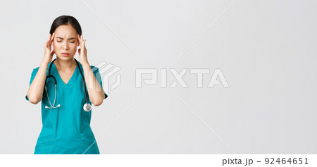 Covid-19, healthcare workers, pandemic concept. Overworked and tired young asian female nurse close eyes, grimacing from headache, feel dizzy, night shift with coronavirus patients, white background 92464651