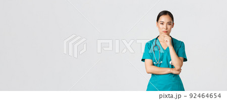 Covid-19, healthcare workers, pandemic concept. Thoughtful female doctor, asian nurse in scrubs looking curious at camera, thinking, searching for solution, standing white background pondering 92464654