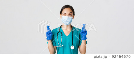 Covid-19, coronavirus disease, healthcare workers concept. Hopeful asian female physician in medical mask and gloves, looking upper left corner and praying, making wish, white background 92464670
