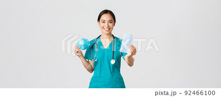 Covid-19, coronavirus disease, healthcare workers concept. Pleasant female physician, asian doctor in scrubs showing respirator and medical mask, provide staff with personal protective equipment Covid-19, coronavirus disease, healthcare workers concept. Pleasant female physician, asian doctor in scrubs showing respirator and medical mask, provide staff with personal protective equipment 92466100