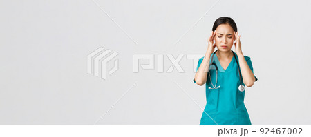 Covid-19, healthcare workers, pandemic concept. Overworked and tired young asian female nurse close eyes, grimacing from headache, feel dizzy, night shift with coronavirus patients, white background Covid-19, healthcare workers, pandemic concept. Overworked and tired young asian female nurse close eyes, grimacing from headache, feel dizzy, night shift with coronavirus patients, white background 92467002