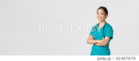 Covid-19, healthcare workers, pandemic concept. Professional confident, smiling asian female doctor, nurse in scrubs with stethoscope for examinations, cross arms and look at camera Covid-19, healthcare workers, pandemic concept. Professional confident, smiling asian female doctor, nurse in scrubs with stethoscope for examinations, cross arms and look at camera 92467079