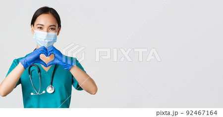 Covid-19, coronavirus disease, healthcare workers concept. Close-up of charming smiling asian female doctor, physician in medical mask and rubber gloves, provide care for patients, show heart gesture Covid-19, coronavirus disease, healthcare workers concept. Close-up of charming smiling asian female doctor, physician in medical mask and rubber gloves, provide care for patients, show heart gesture 92467164