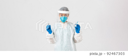 Covid-19, coronavirus disease, healthcare workers concept. Amazed and excited female asian doctor, infectionist in personal protective equipment, holding syringe and ampoule with vaccine 92467303