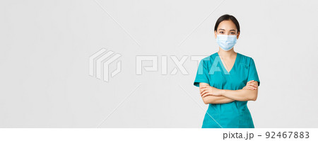 Covid-19, coronavirus disease, healthcare workers concept. Smiling confident asian female doctor, physician making checkup, wearing scrubs and medical mask, looking determined, white background Covid-19, coronavirus disease, healthcare workers concept. Smiling confident asian female doctor, physician making checkup, wearing scrubs and medical mask, looking determined, white background 92467883