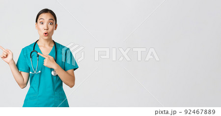 Covid-19, healthcare workers, pandemic concept. Impressed and amazed female asian nurse in scrubs asking question with intrigued expression. Doctor looking thrilled and pointing upper left corner Covid-19, healthcare workers, pandemic concept. Impressed and amazed female asian nurse in scrubs asking question with intrigued expression. Doctor looking thrilled and pointing upper left corner 92467889