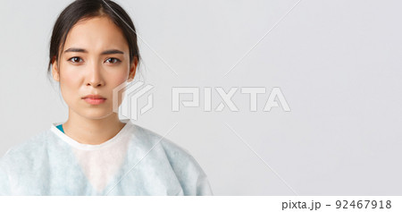 Covid-19, coronavirus disease, healthcare workers concept. Serious exhausted asian female doctor looking tired after shift at hospital, take-off personal protective equipment, have skin marks 92467918