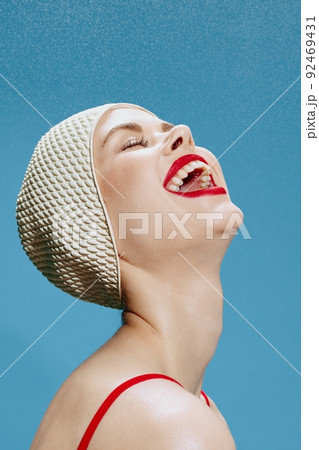 Joyful happy girl in a swimming cap catches the rain from above with her mouth open, posing with her eyes closed on a blue background. Close portrait of an emotional woman Joyful happy girl in a swimming cap catches the rain from above with her mouth open, posing with her eyes closed on a blue background. Close portrait of an emotional woman 92469431