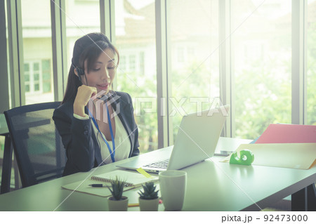 Asian female operator is talking on the phone to service client in the telemarkerting office. Asian female operator is talking on the phone to service client in the telemarkerting office. 92473000