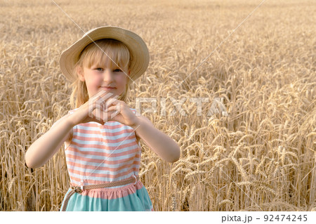 Blond Girl looks at the camera and Shows the Heart of her Hands in the wheat field . Blond Girl looks at the camera and Shows the Heart of her Hands in the wheat field . 92474245