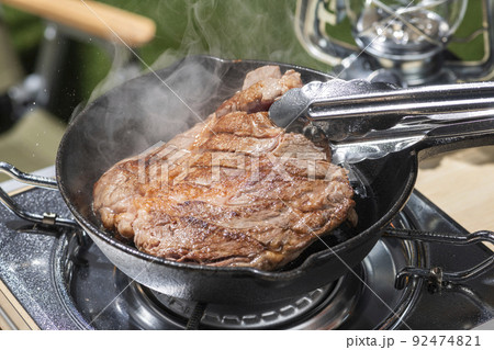 アウトドアのキャンプ場でスキレットを使ってステーキ肉を焼く 92474821