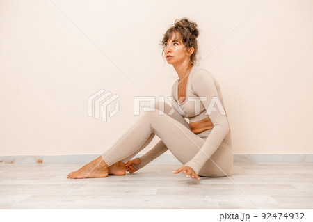 Well looking middle aged woman with long hair, fitness instructor in beige sportswear, doing stretching and pilates on yoga mat in the gym. Healthy lifestyle, harmony. Female fitness yoga meditation. 92474932