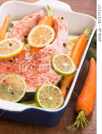 Raw fish is ready for baking. Salmon steak. Red fish and sliced lemons on white Raw fish is ready for baking. Salmon steak. Red fish and sliced lemons on white 92475157