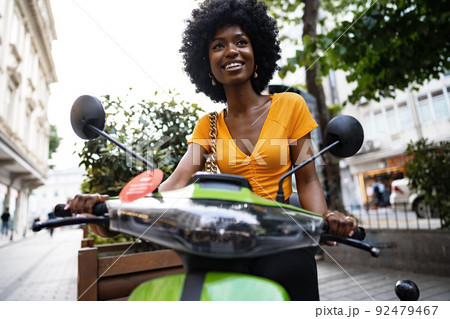 Portrait of young african american woman riding green motorbike in the city Portrait of young african american woman riding green motorbike in the city 92479467