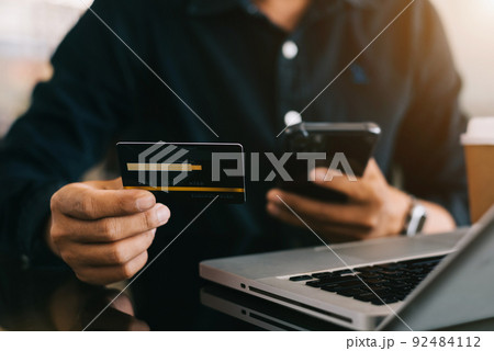 Closeup male holding hand credit card. Businessman use smartphone online payments shopping touching screen mobile phone name numbers. Closeup male holding hand credit card. Businessman use smartphone online payments shopping touching screen mobile phone name numbers. 92484112