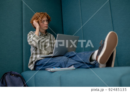 Ginger boy sitting with a laptop and watching something online 92485135