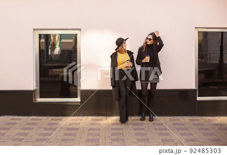 Two stylish women female friends enjoying nice talk and drinking take away coffee outdoors 92485303